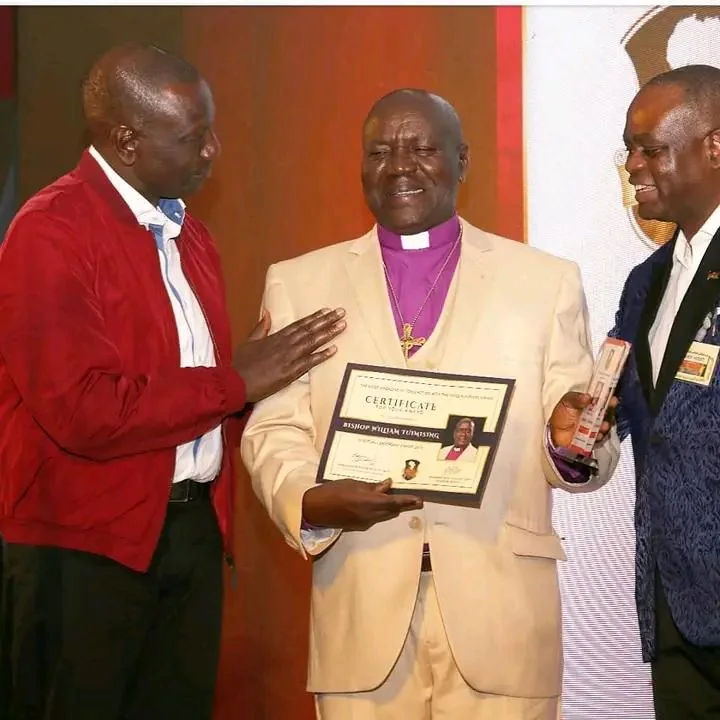 Bishop William Tuimising holding a framed certificate of honour at an awards ceremony