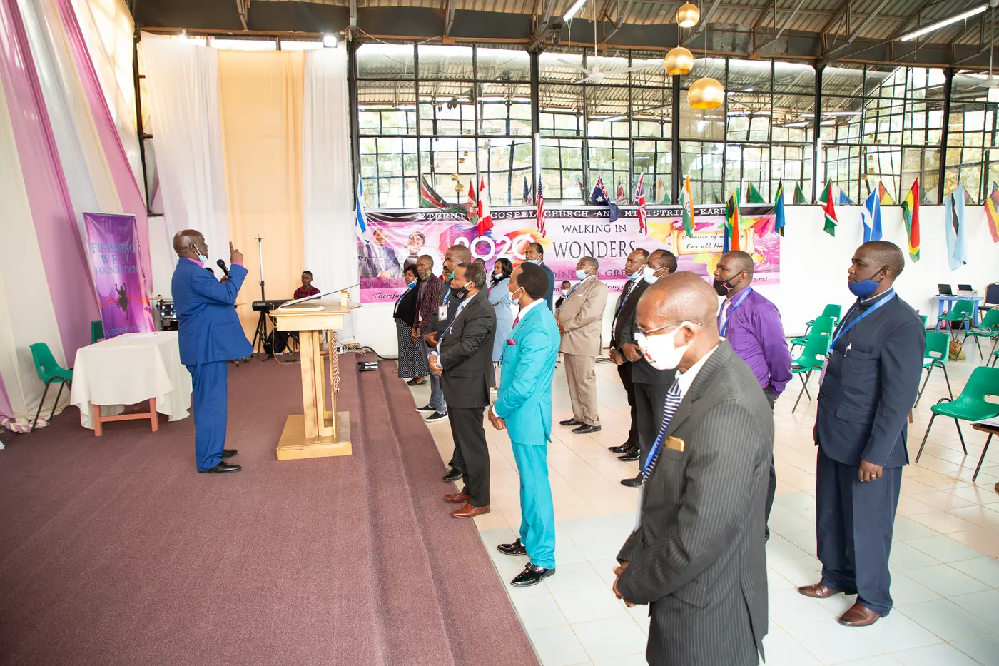 Spiritual leaders standing in prayer in a church hall while a minister prays at the pulpit