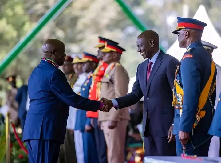 A formal handshake at a national ceremony with uniformed officers standing behind